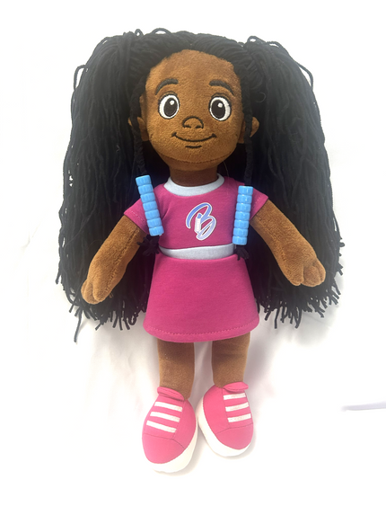 A plush Bead Barrettes  doll with medium brown skin, large cartoon eyes, and long black yarn hair. The doll is wearing two Bead Barrettes, a pink dress with a white collar, blue shoulder straps, and pink sneakers with white stripes, set against a plain white background.